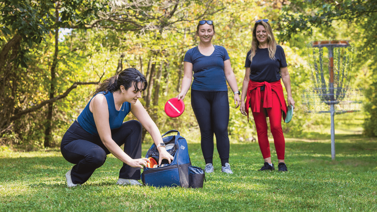 Group of women playing disc golf on a sunny day at Mosquito Lake State Park in Northeast Ohio, surrounded by forest and open green space