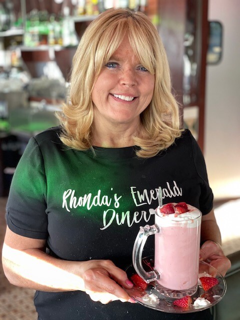 Rhonda from Rhonda's Emerald Diner holding a strawberry milkshake.