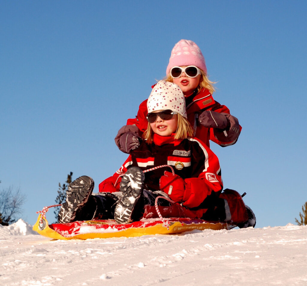 Two girls sledding down a snowy hill in Trumbull County, Northeast Ohio, enjoying a fun winter day outdoors with scenic countryside views.