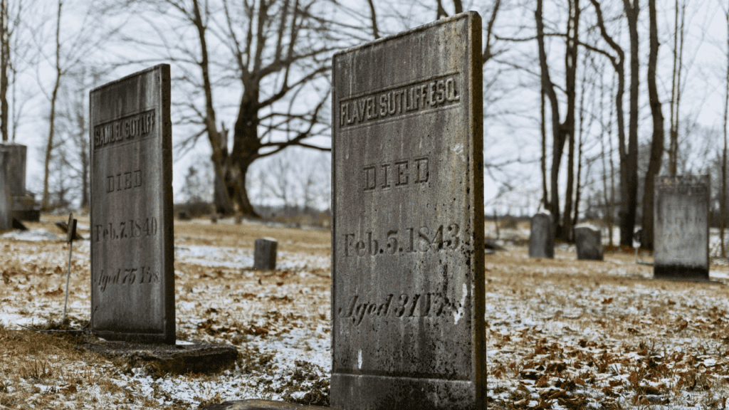 Historic headstones at Vernon Cemetery in Trumbull County, Ohio, are lightly dusted with winter snow among bare trees and quiet scenery.