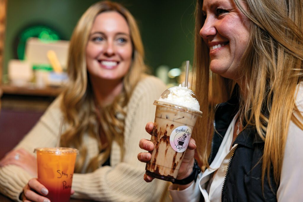 Two women enjoying coffee and tea drinks at Broken Leaf Café in Newton Falls, Ohio - a cozy Trumbull County coffee shop serving handcrafted lattes, iced teas, and sweet treats.