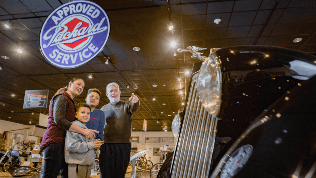 Family viewing classic Packard automobile at the National Packard Museum in Warren, Ohio, under vintage Approved Packard Service sign