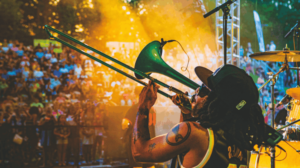 Musician playing trombone on stage during River Rock at the Amp summer concert in Warren, Ohio, with a large crowd in the background