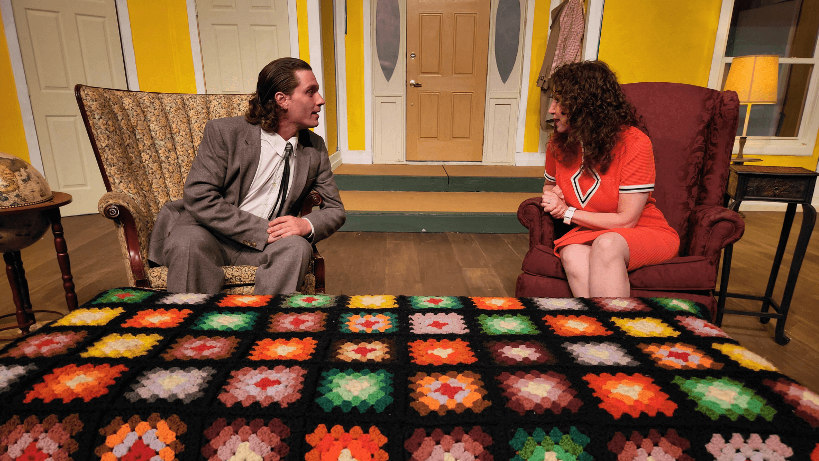Two actors speak from vintage armchairs on a colorful set with a crochet Afghan at Trumbull New Theatre in Niles, Ohio.