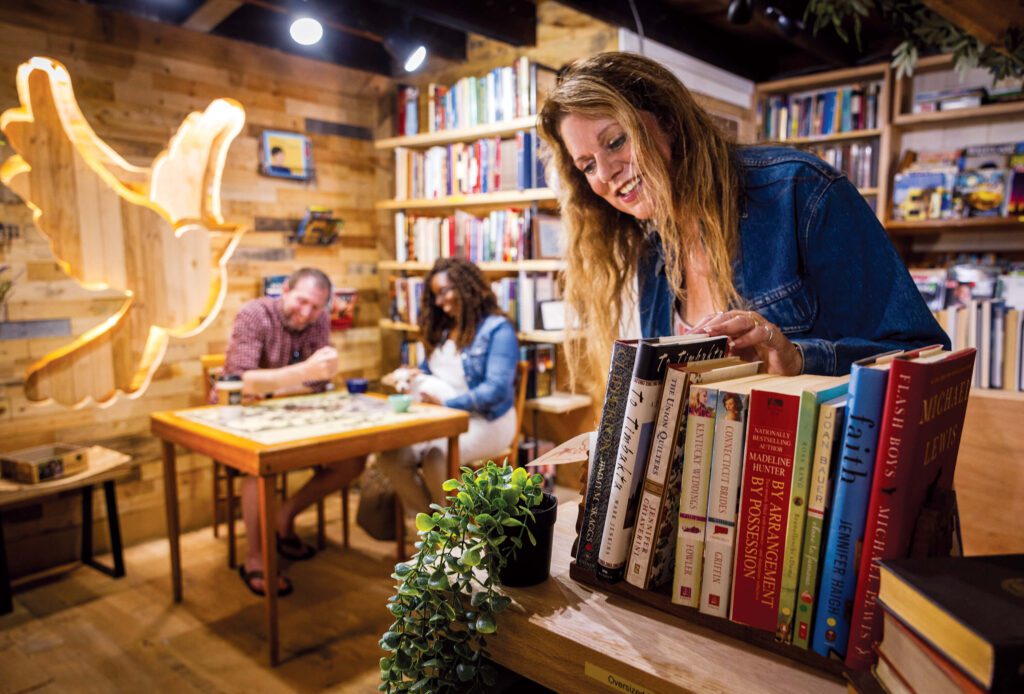Customer browsing shelves at Papa’s Book Shoppe, an independent bookstore in Cortland, Trumbull County, Northeast Ohio; warm wood interior with reading/game area.