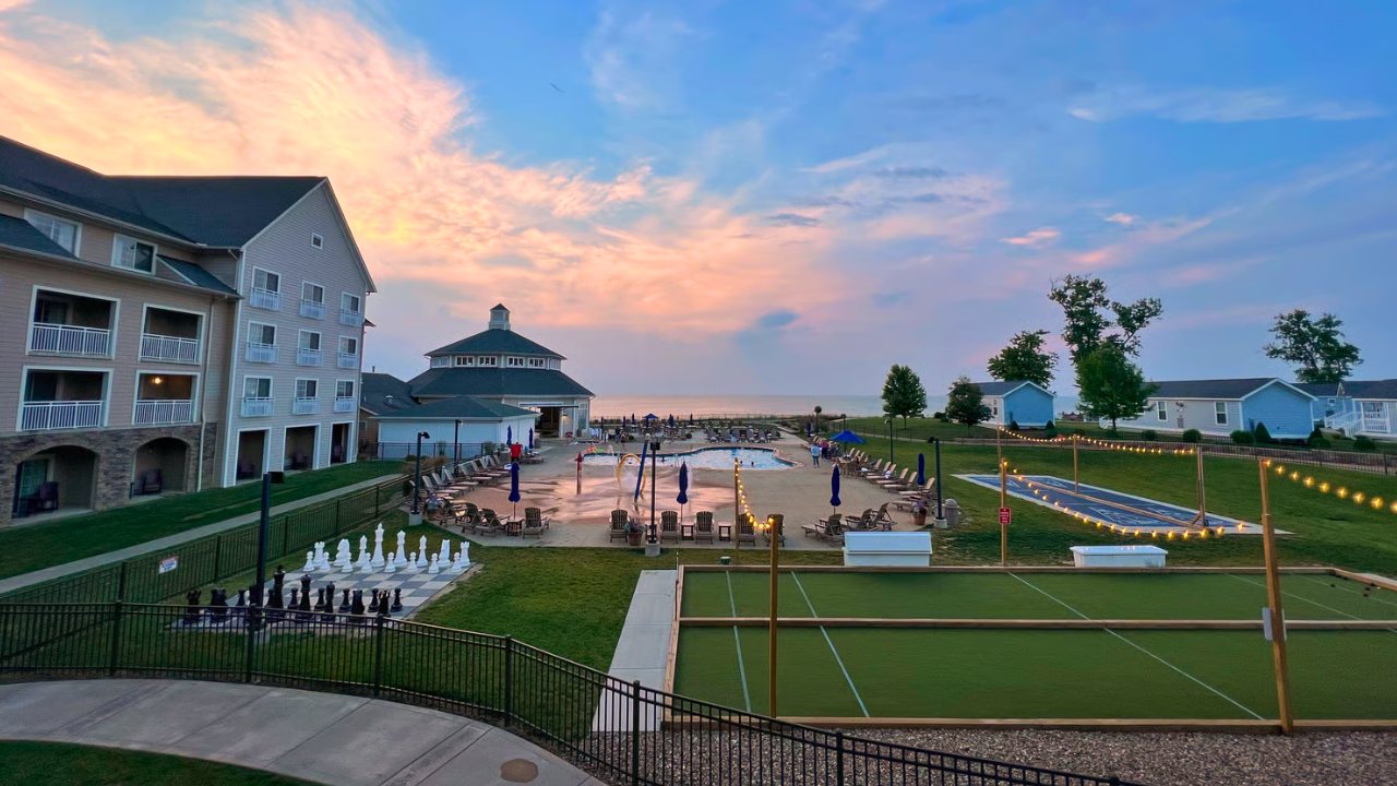 Sunset view of The Lodge at Geneva-on-the-Lake on Lake Erie, featuring the outdoor pool, string lights, bocce and shuffleboard courts, and nearby cottages in Ashtabula County, Ohio.
