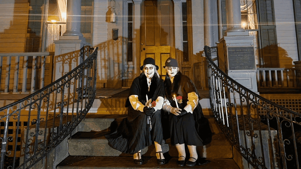 Two actors with vintage attire sit on the front steps of the Harriet Taylor Upton House, holding roses and candles during the Warren Ghost Walk in Warren, Ohio.