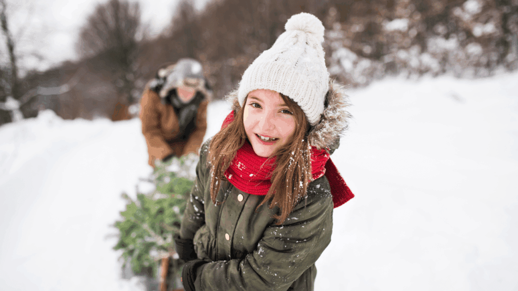 Smiling child in a red scarf pulls a freshly cut Christmas tree on a sled at Bradley Tree Farm in Vienna, Trumbull County, Ohio—family cut-your-own holiday outing in Northeast Ohio.