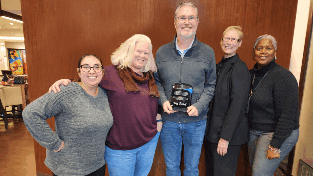 Group photo in Warren, Ohio of Trumbull County Tourism staff presenting an appreciation award to Jordan Taylor of the Mahoning Valley Scrappers for board leadership.