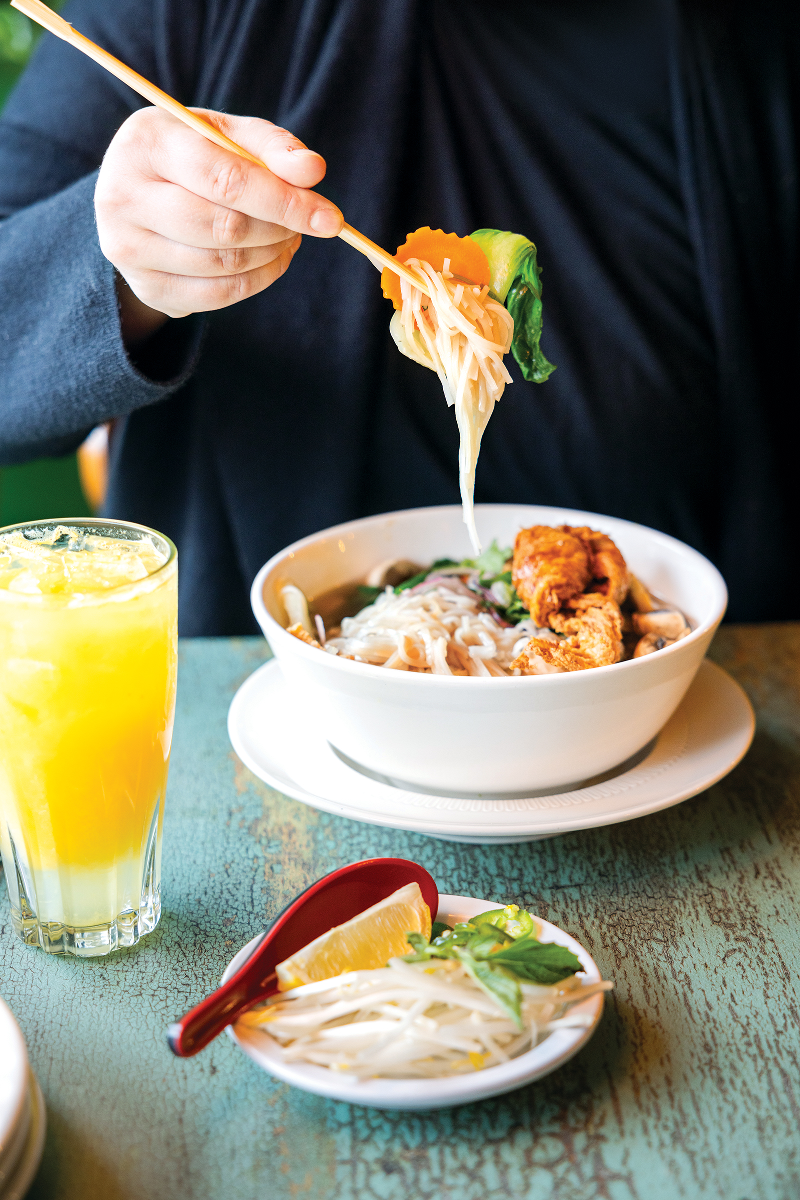 an's House vietnemanese comfort food, a young woman picks up wamr pho with chopsticks
