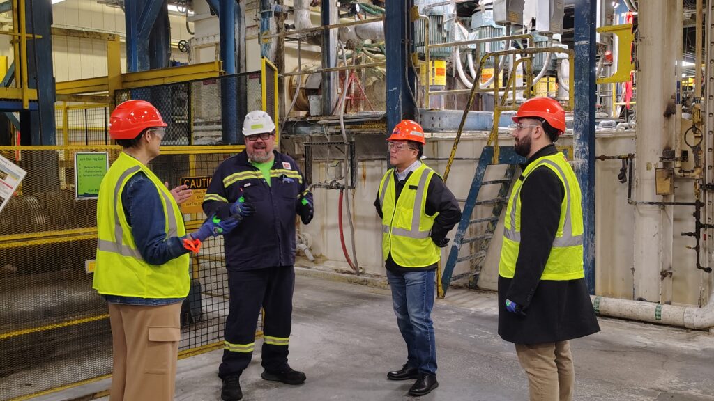 Four people standing in reflective jackets and hard hats at the Novelis facility.