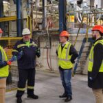 Four people standing in reflective jackets and hard hats at the Novelis facility.